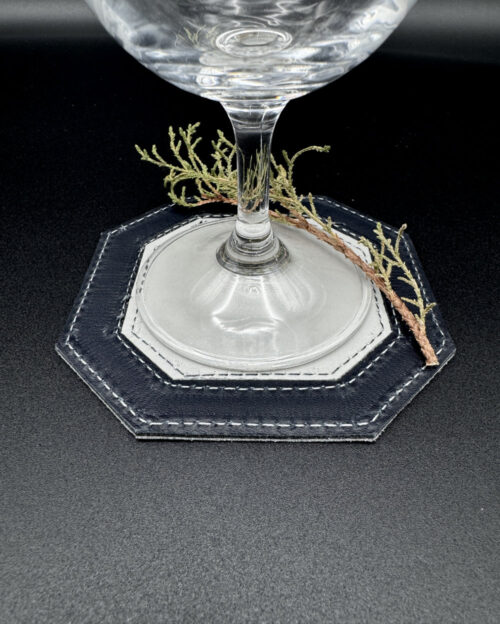 Leather coaster in an octagon shape with the center in white and the outside trim in navy with a glass on top
