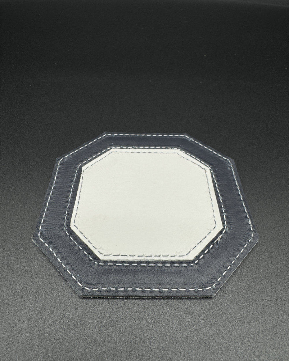 Leather coaster in an octagon shape with the center in white and the outside trim in navy